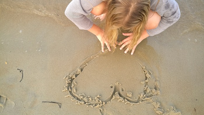 Flicka som ritar ett hjärta i sanden på en strand