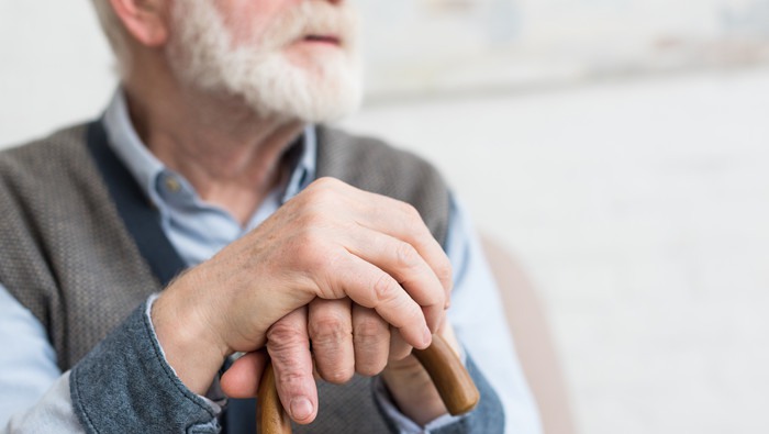Cropped view of elderly man with walking stick in hands