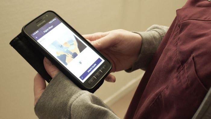 Omsorgspersonal håller en mobiltelefon i handen som visar hur appen till de digitala trygghetslarmen ser ut.