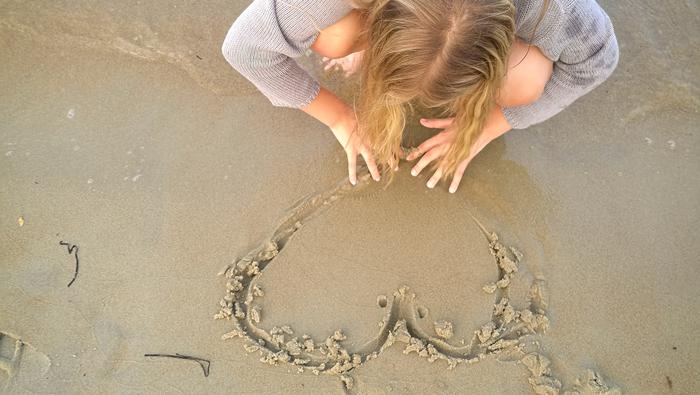 Flicka som ritar i sanden