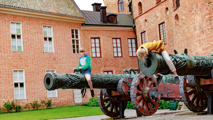 Två barn som sitter på varsin kanon framför Gripsholms slott.