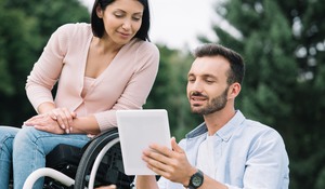 happy disabled woman and smiling boyfriend using digital tablet in park