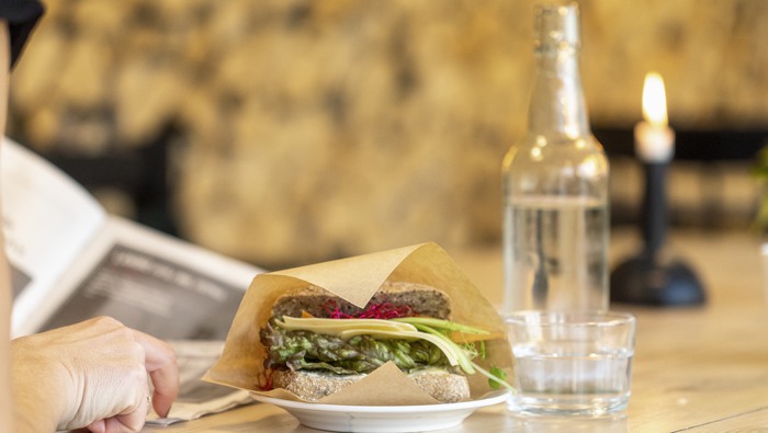 Smörgås fika på ett bord, person som läser tidning, på Printz bageri Gula Industrihuset 